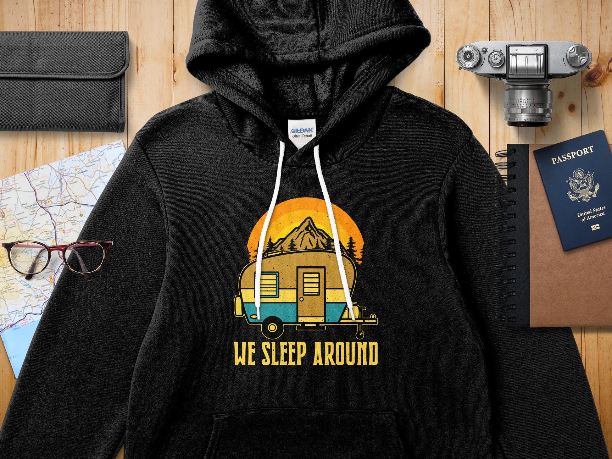Black hoodie with a retro camper and sunset graphic and "We Sleep Around" text.