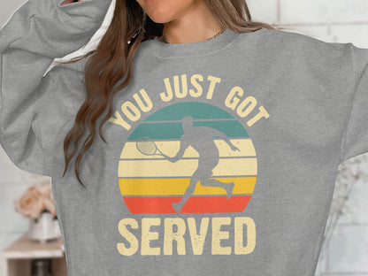Grey sweatshirt with "YOU JUST GOT SERVED" and a tennis player silhouette against a striped sunset.