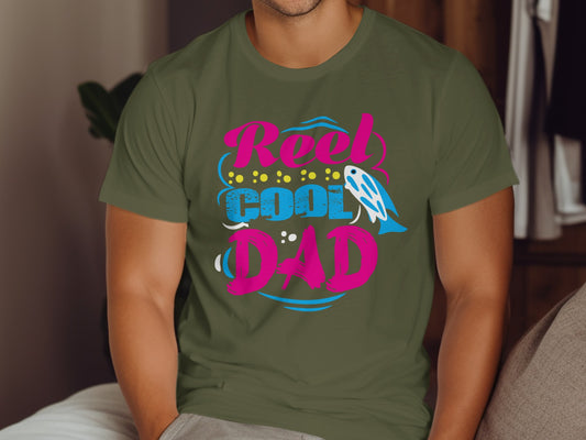 "Reel Cool Dad" text with fishing lure graphic on olive green t-shirt.