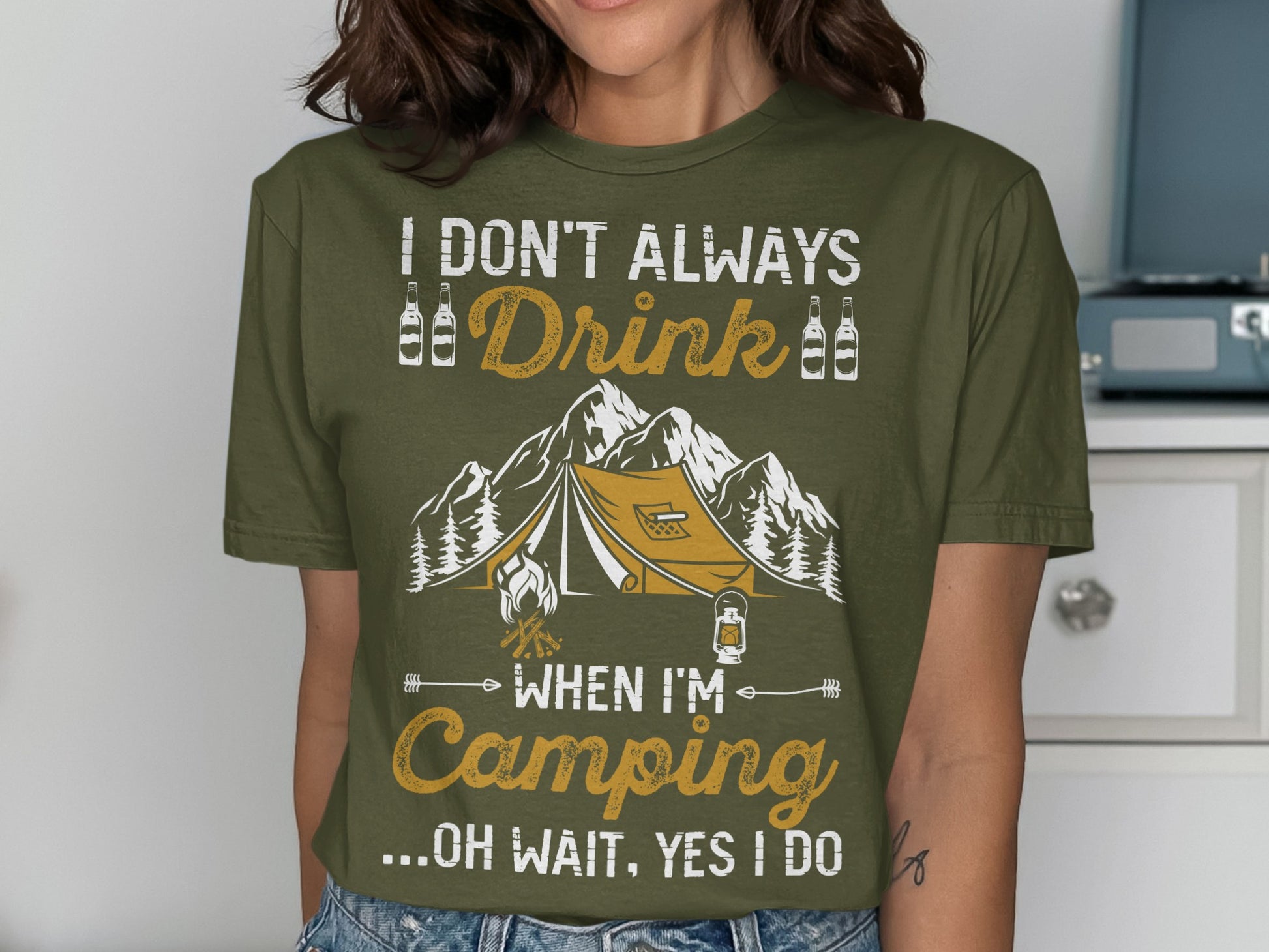 Olive green t-shirt with tent and mountain graphic and text.
