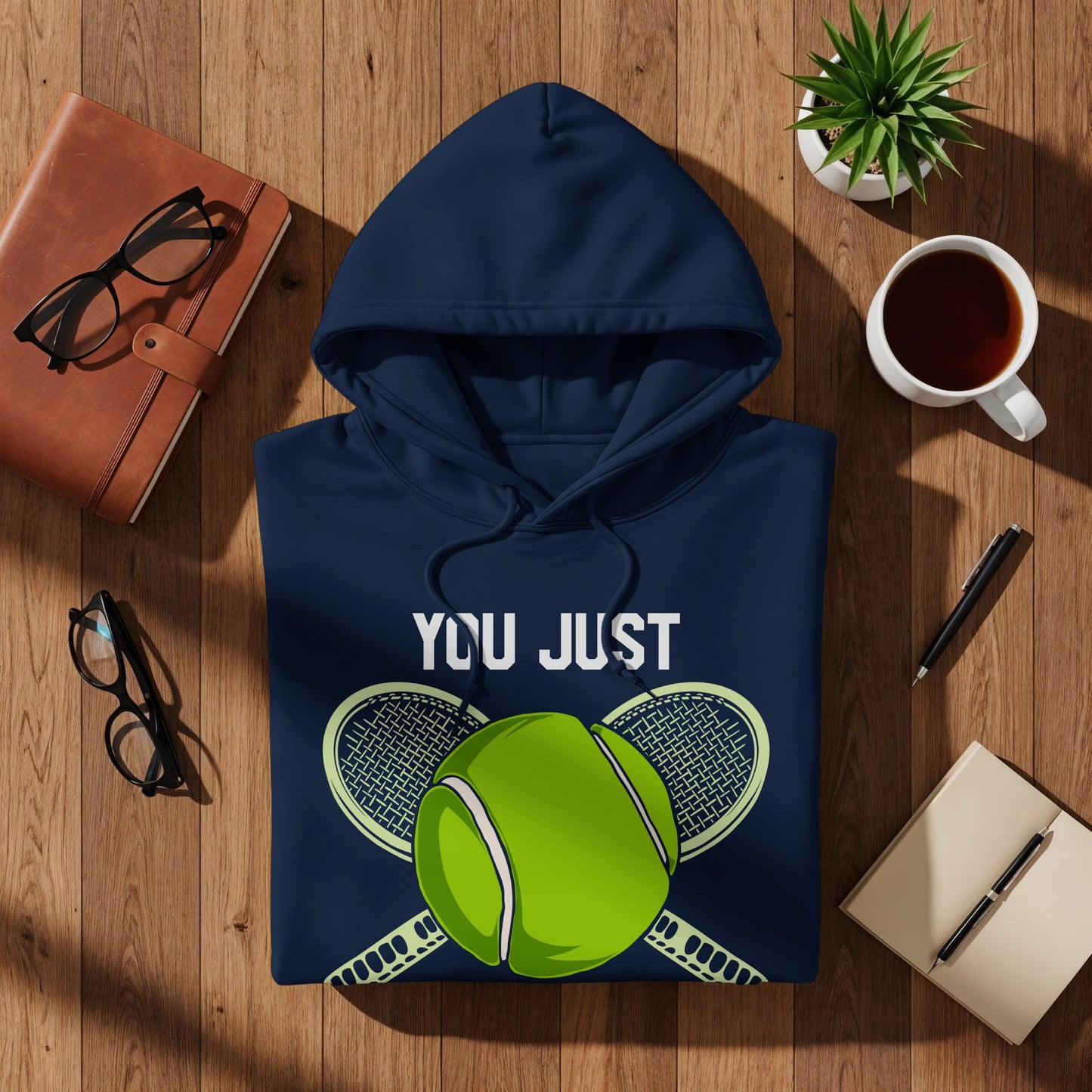 Navy hoodie with "YOU JUST" and tennis graphic, on wooden surface.