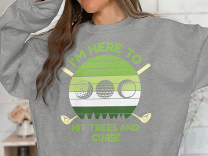 Grey sweatshirt with "I'm here to hit trees and curse" text and golf balls.