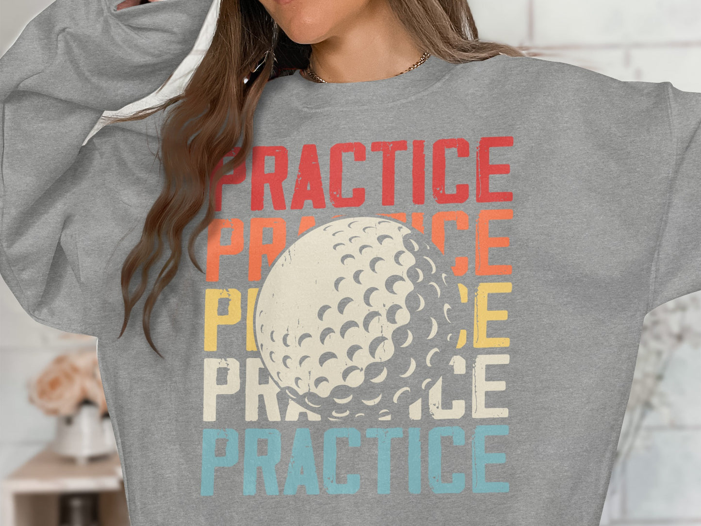 Woman wearing gray sweatshirt with "PRACTICE" text and golf ball graphic.