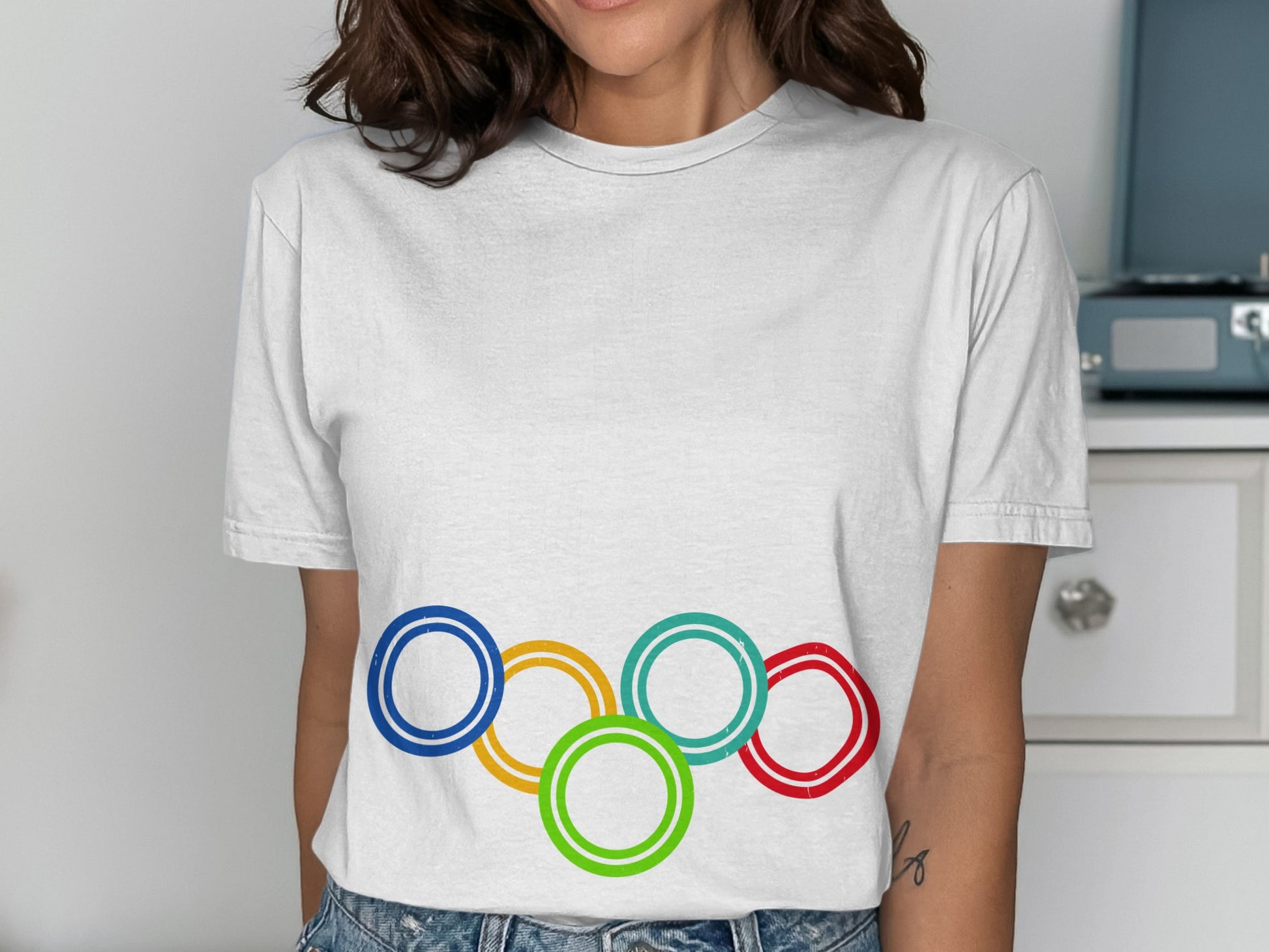 White t-shirt featuring the Olympic rings in blue, yellow, green, and red.
