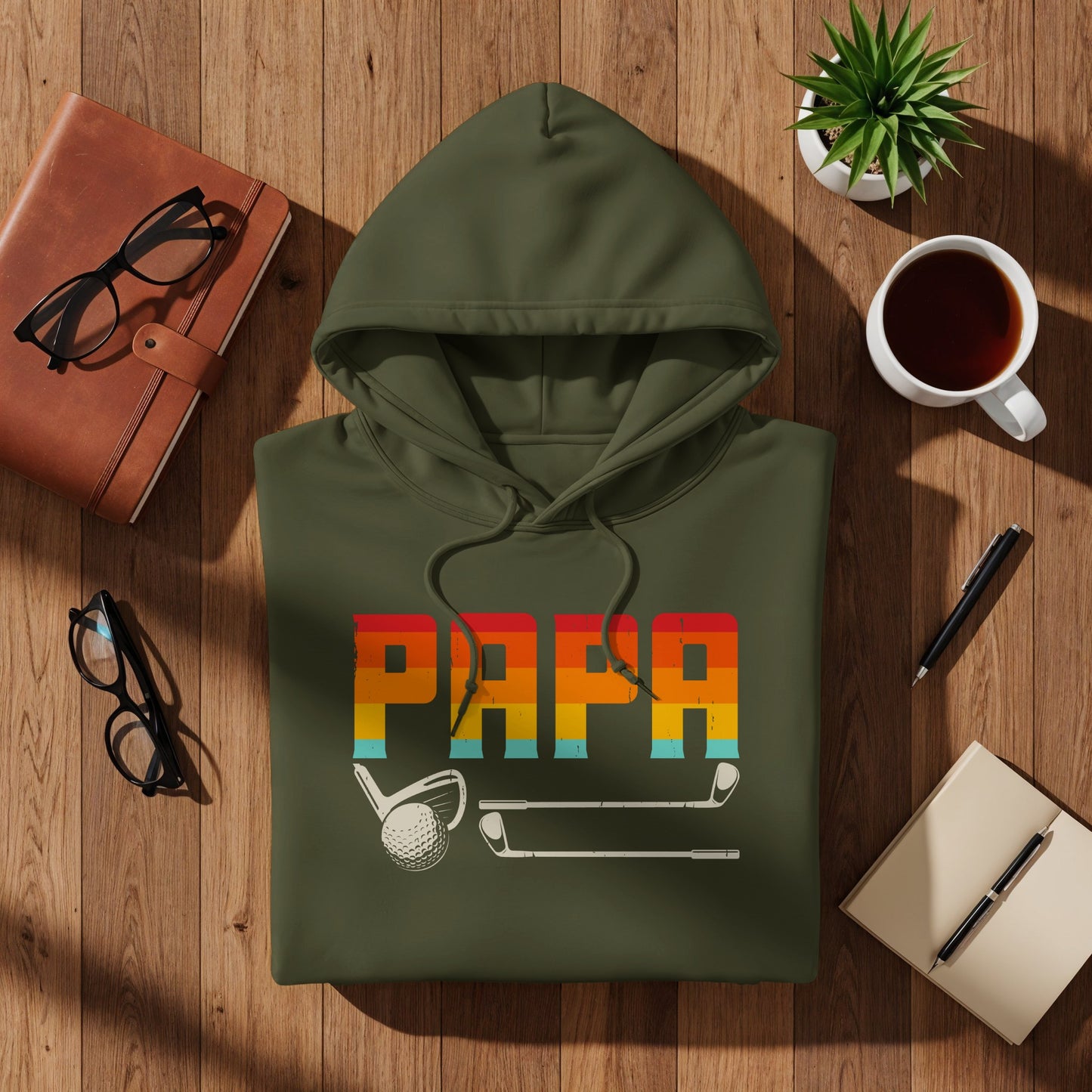 Green hoodie with "PAPA" text, golf clubs, and coffee on wooden table.