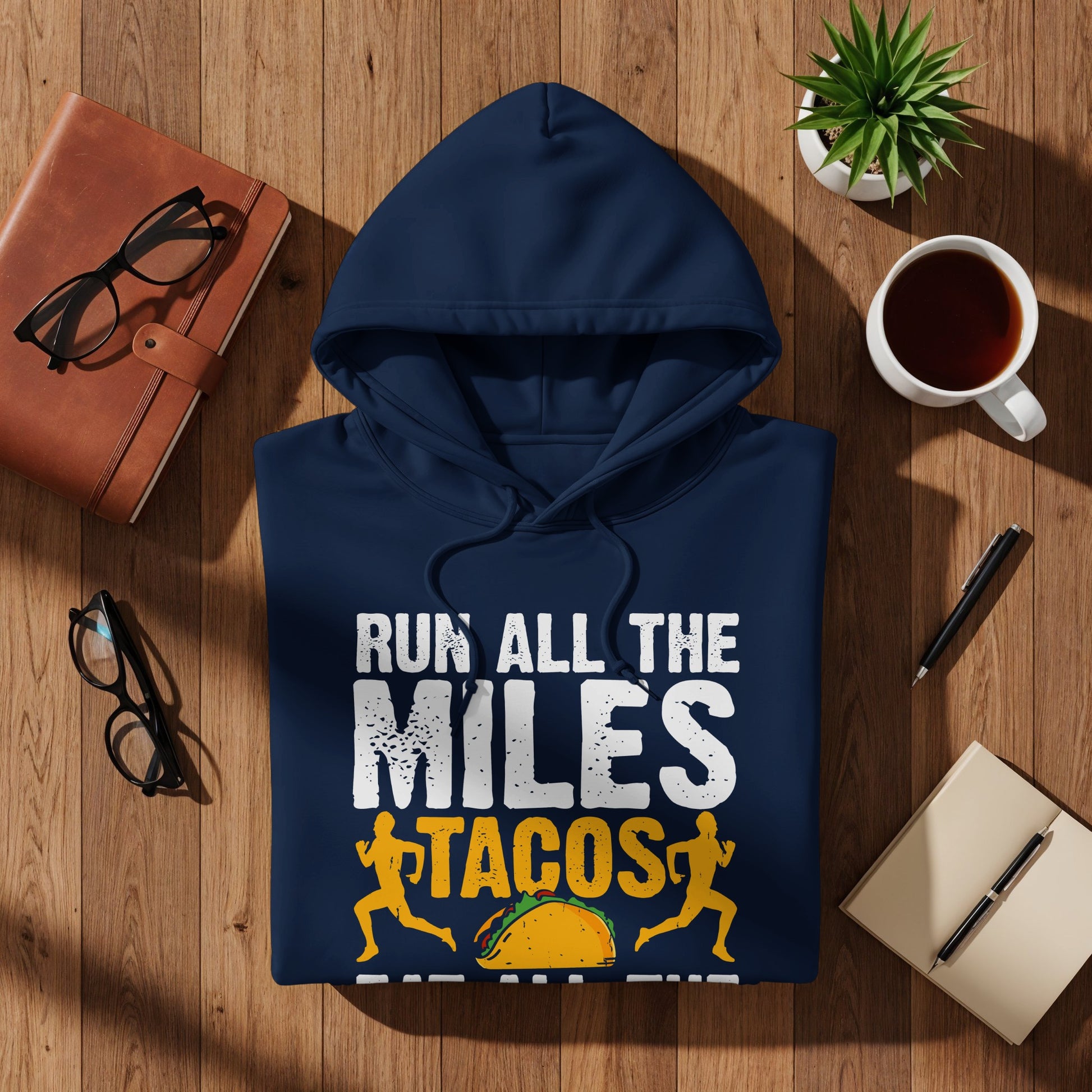 Navy hoodie with "Run All The Miles Tacos" graphic on a wooden surface.