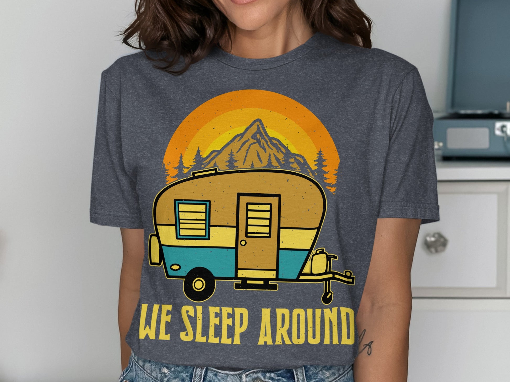 T-shirt with graphic of a camper trailer and mountains, text reads "WE SLEEP AROUND".