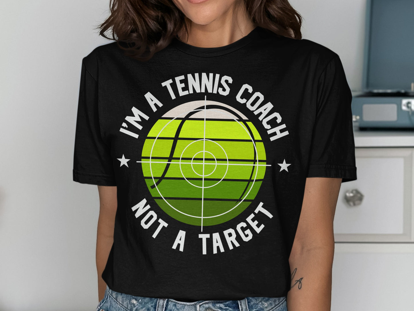 Black t-shirt with "I'M A TENNIS COACH NOT A TARGET" and tennis ball graphic.