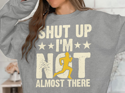 Gray sweatshirt with "SHUT UP I'M ALMOST THERE" and running silhouette.