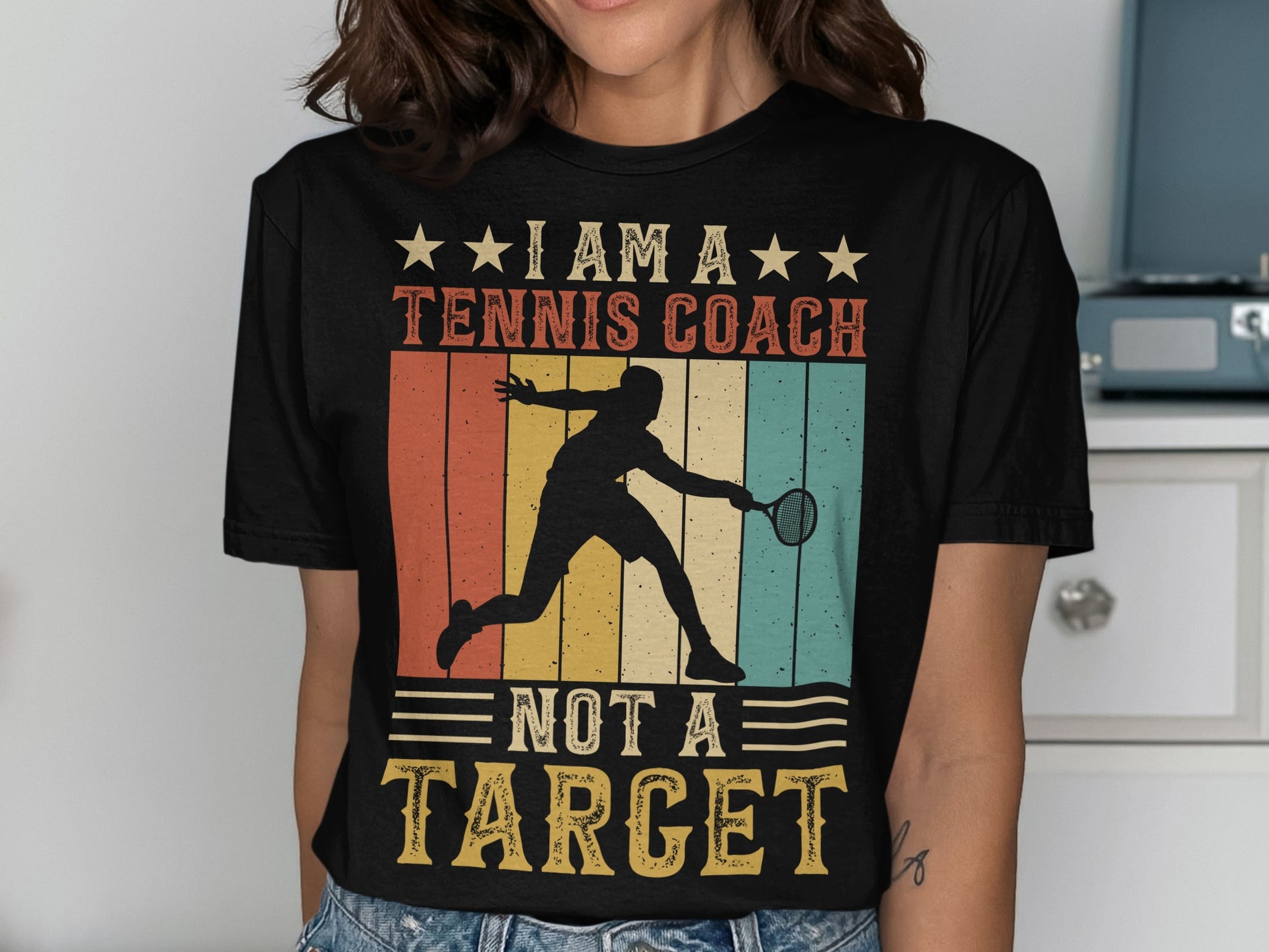 Black t-shirt with "I am a tennis coach, not a target" text and graphic.