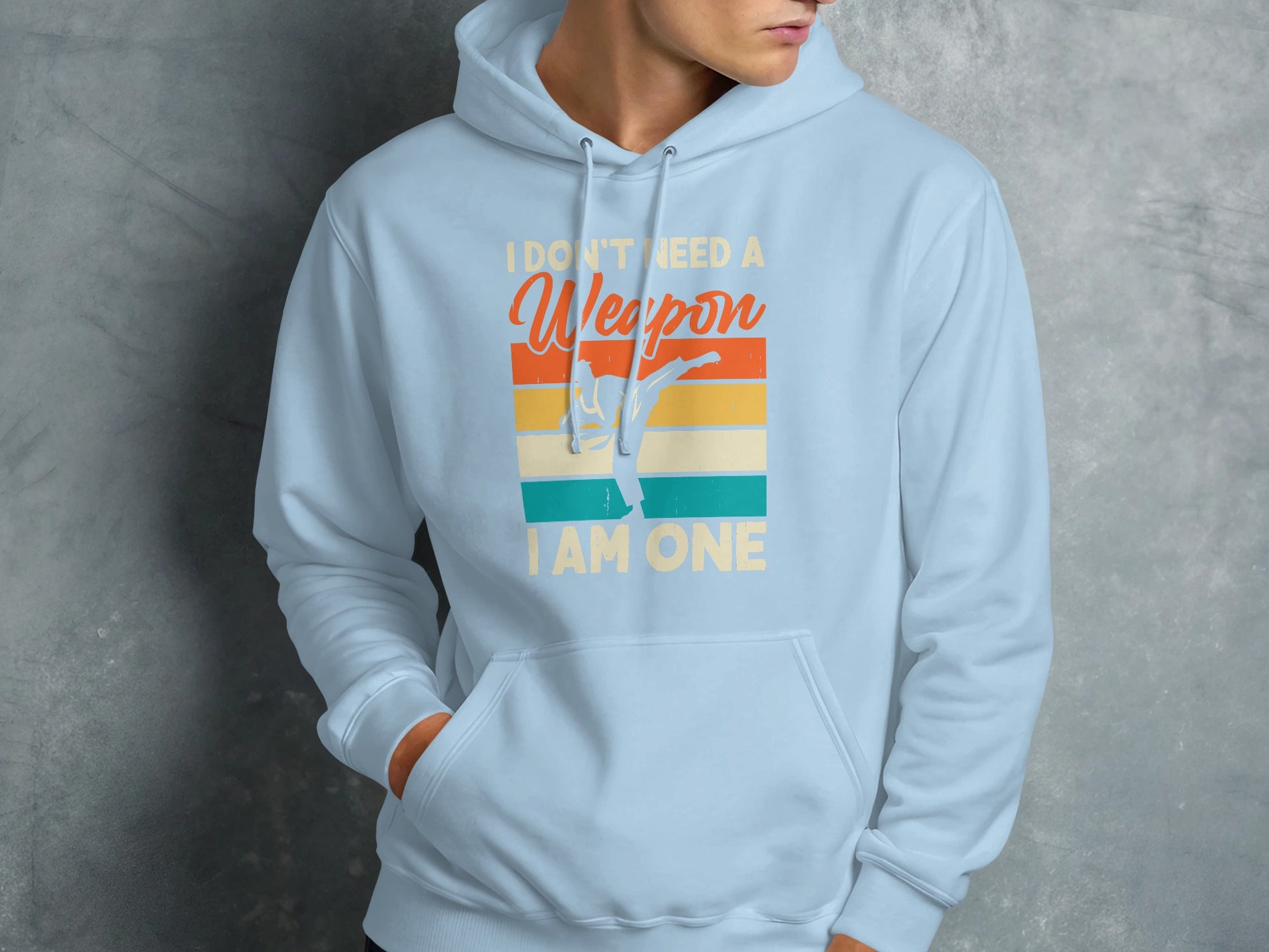 Light blue hoodie with "I Don't Need A Weapon I Am One" text and martial artist graphic.