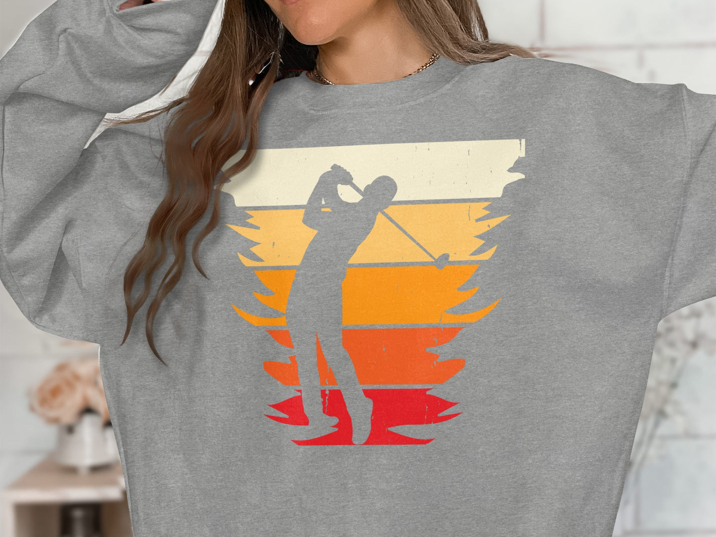 Golfer swinging club against a retro sunset background on a gray sweatshirt.