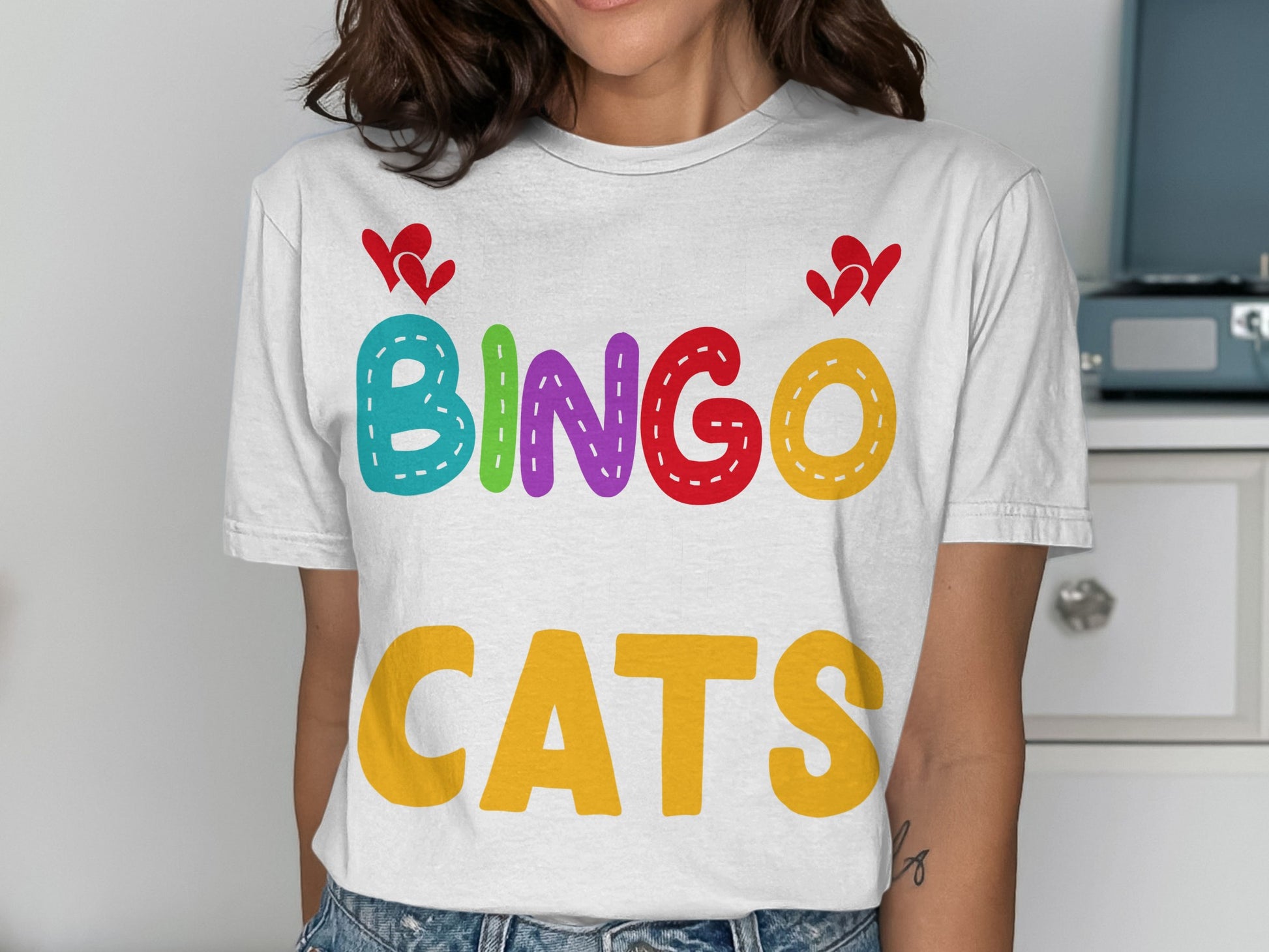 White t-shirt with "BINGO CATS" in colorful bubbly letters and red hearts.