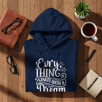 Navy hoodie with "Everything Starts With A Dream" text on wooden surface.