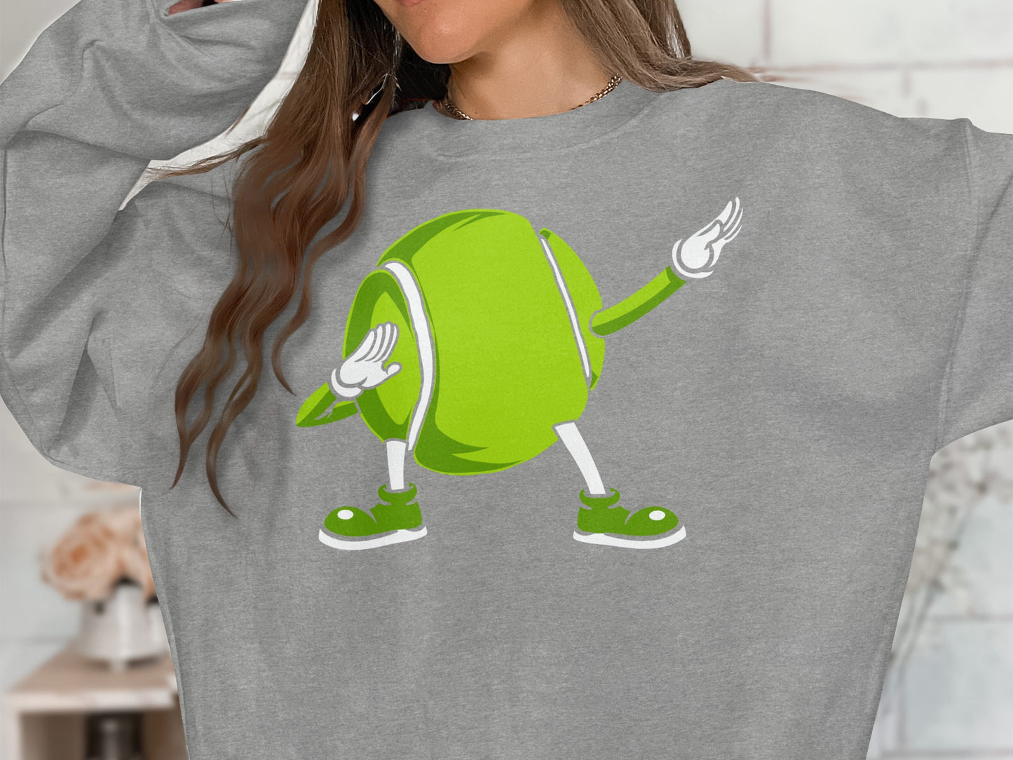 Cartoon tennis ball character in a dab pose on a gray sweatshirt.