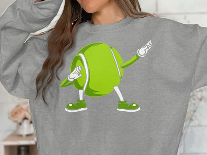 Cartoon tennis ball character in a dab pose on a gray sweatshirt.