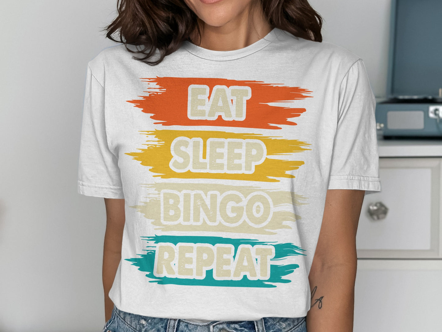 White t-shirt with "Eat Sleep Bingo Repeat" text in colorful stripes.