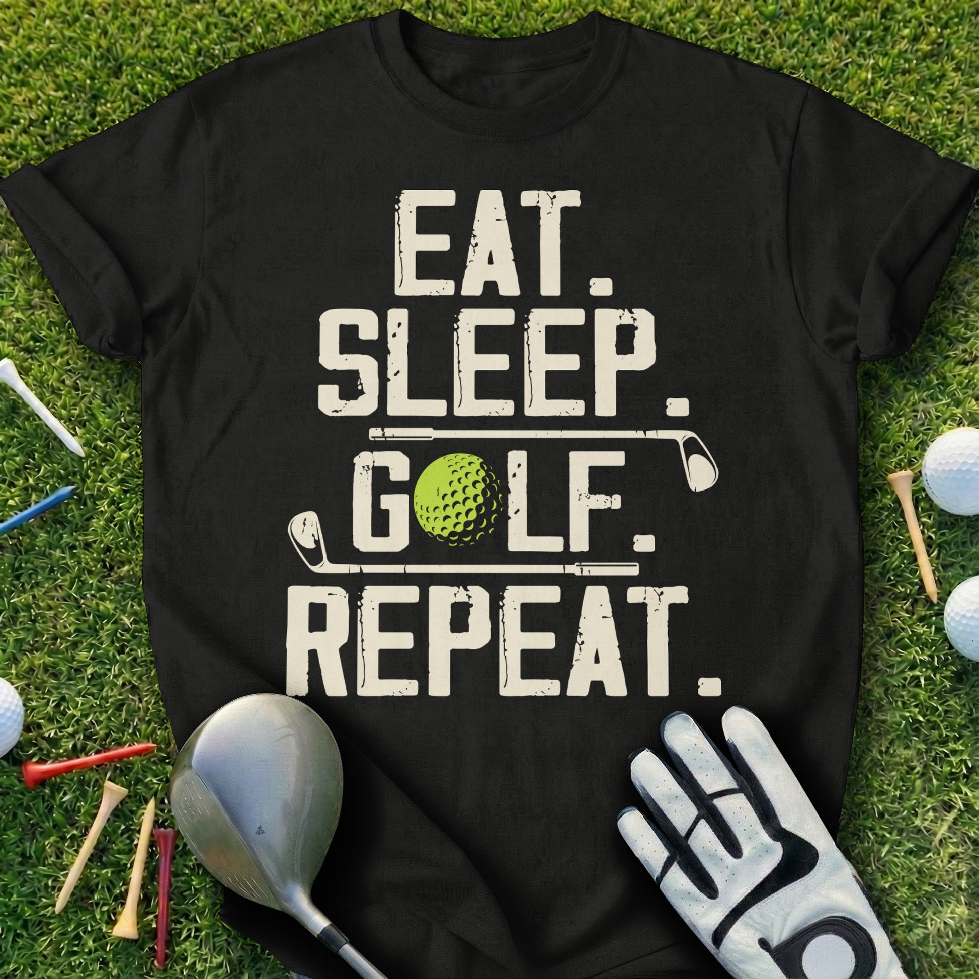 Black t-shirt with "Eat. Sleep. Golf. Repeat." text and golf accessories on grass.