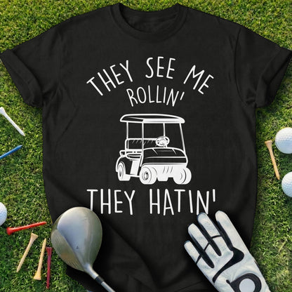 Black t-shirt with white graphic of golf cart and text "They see me rollin' they hatin'".