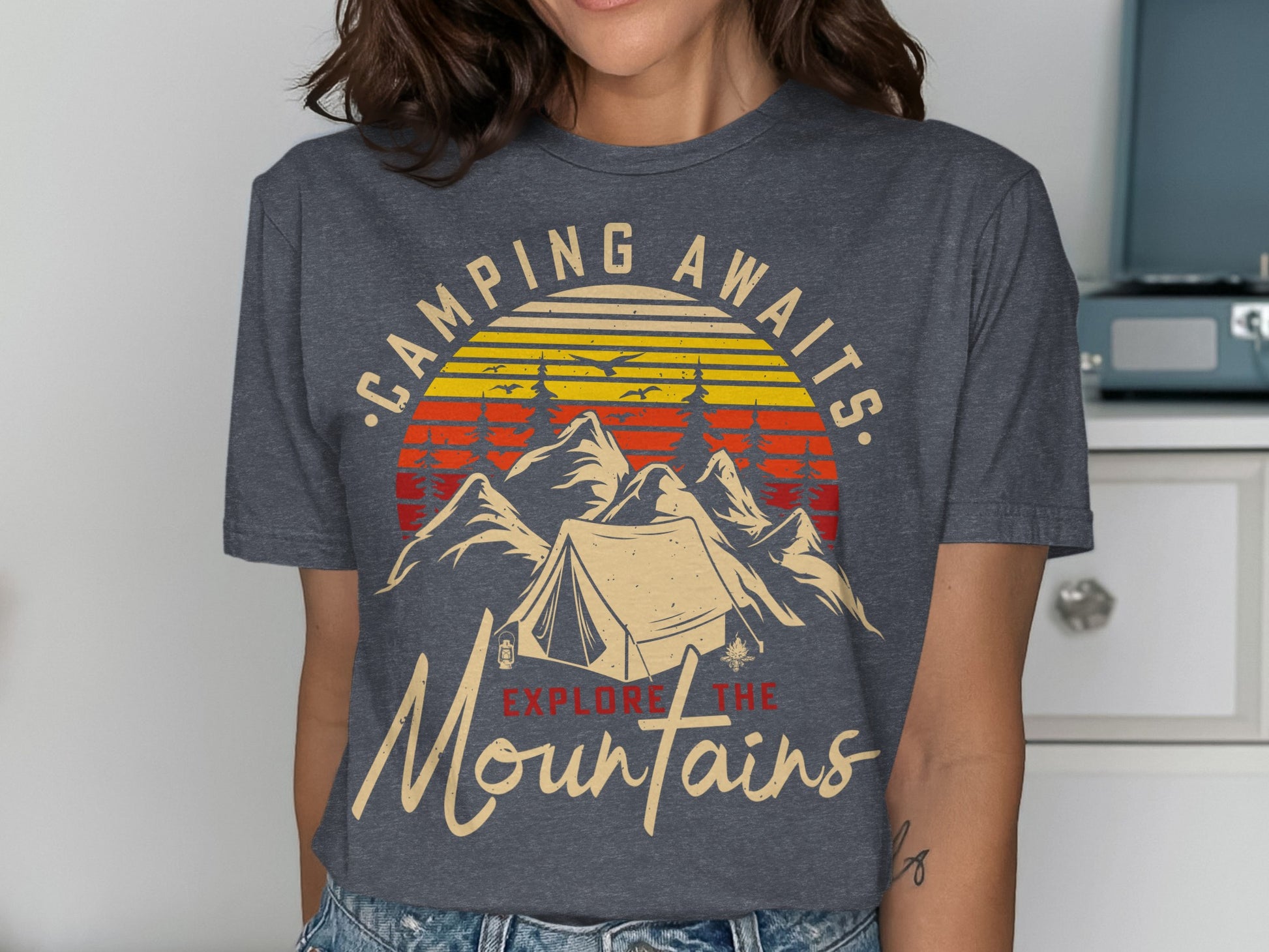 T-shirt with mountain camping graphic and text "CAMPING AWAITS. EXPLORE THE Mountains".