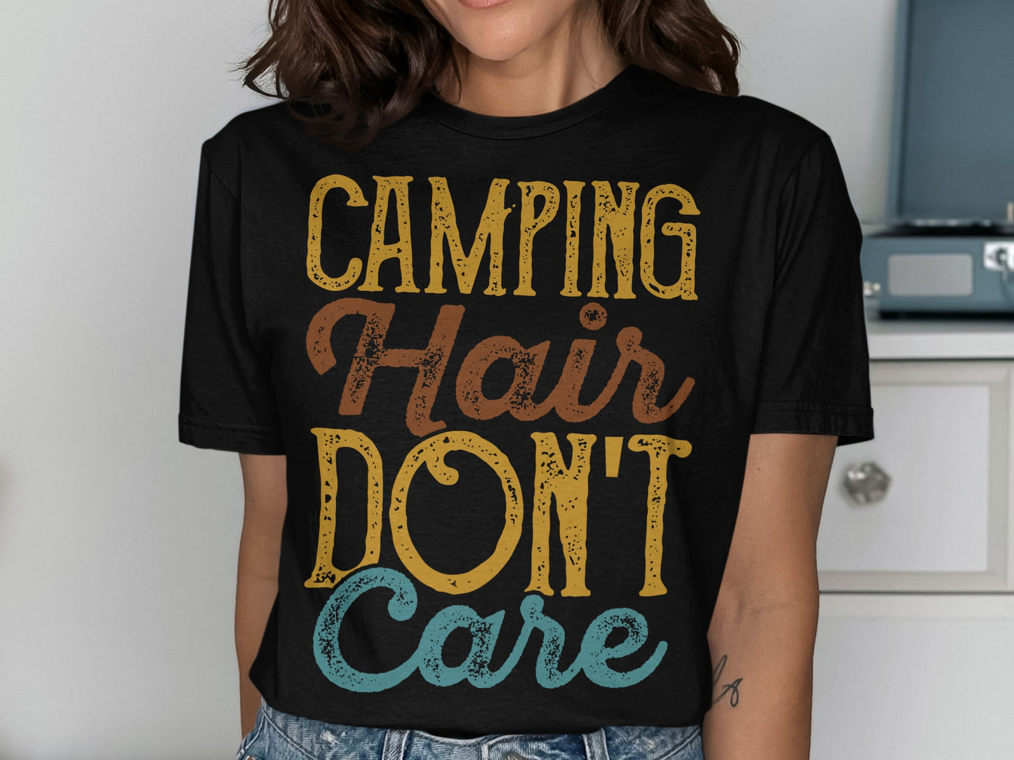 Black t-shirt with "CAMPING Hair DON'T Care" in distressed yellow, brown, and blue lettering.