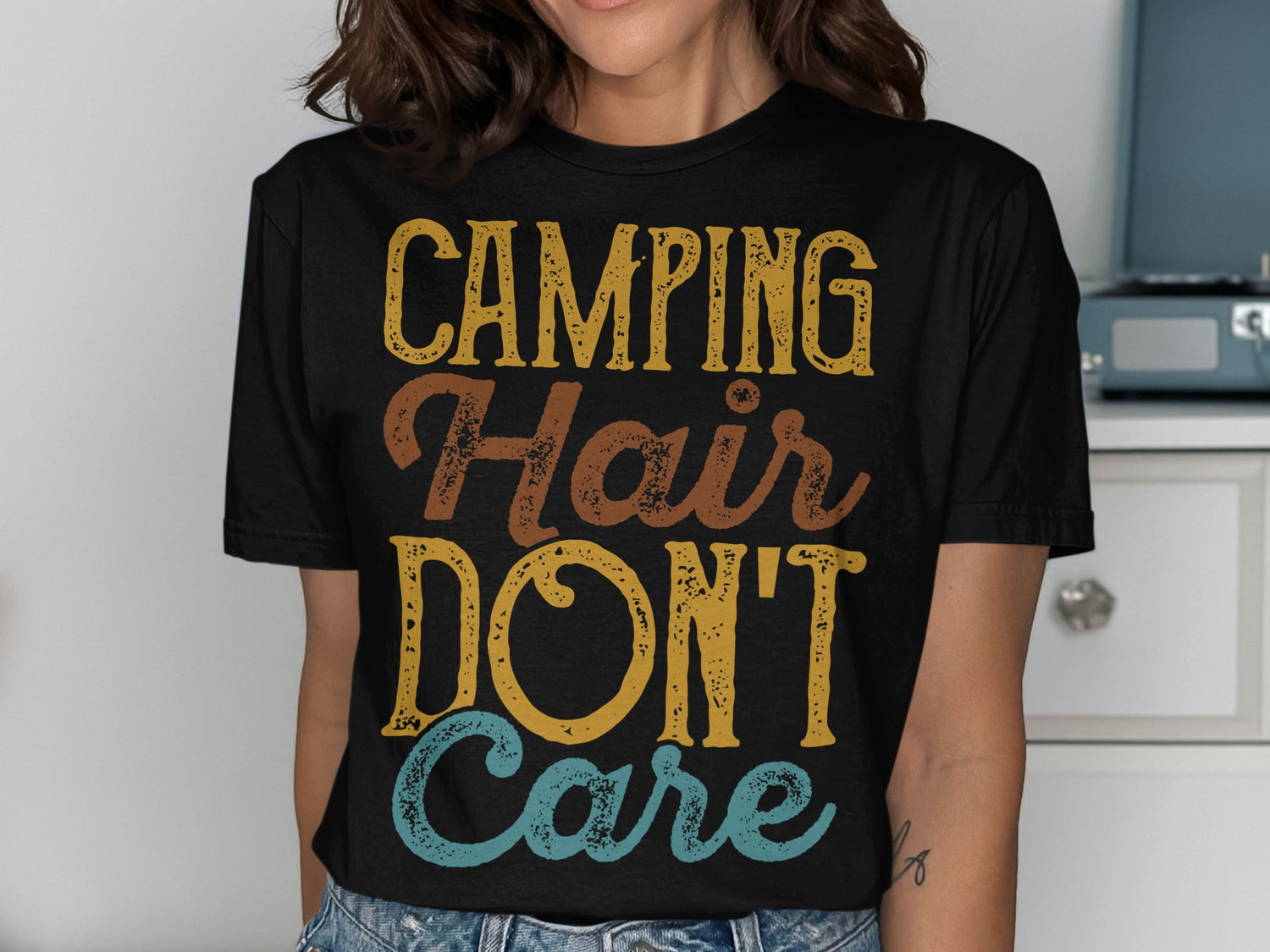 Black t-shirt with "CAMPING Hair DON'T Care" in distressed yellow, brown, and blue lettering.