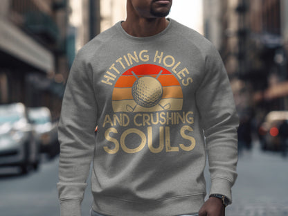 Gray sweatshirt with "Hitting Holes And Crushing Souls" text and golf ball sunset graphic.