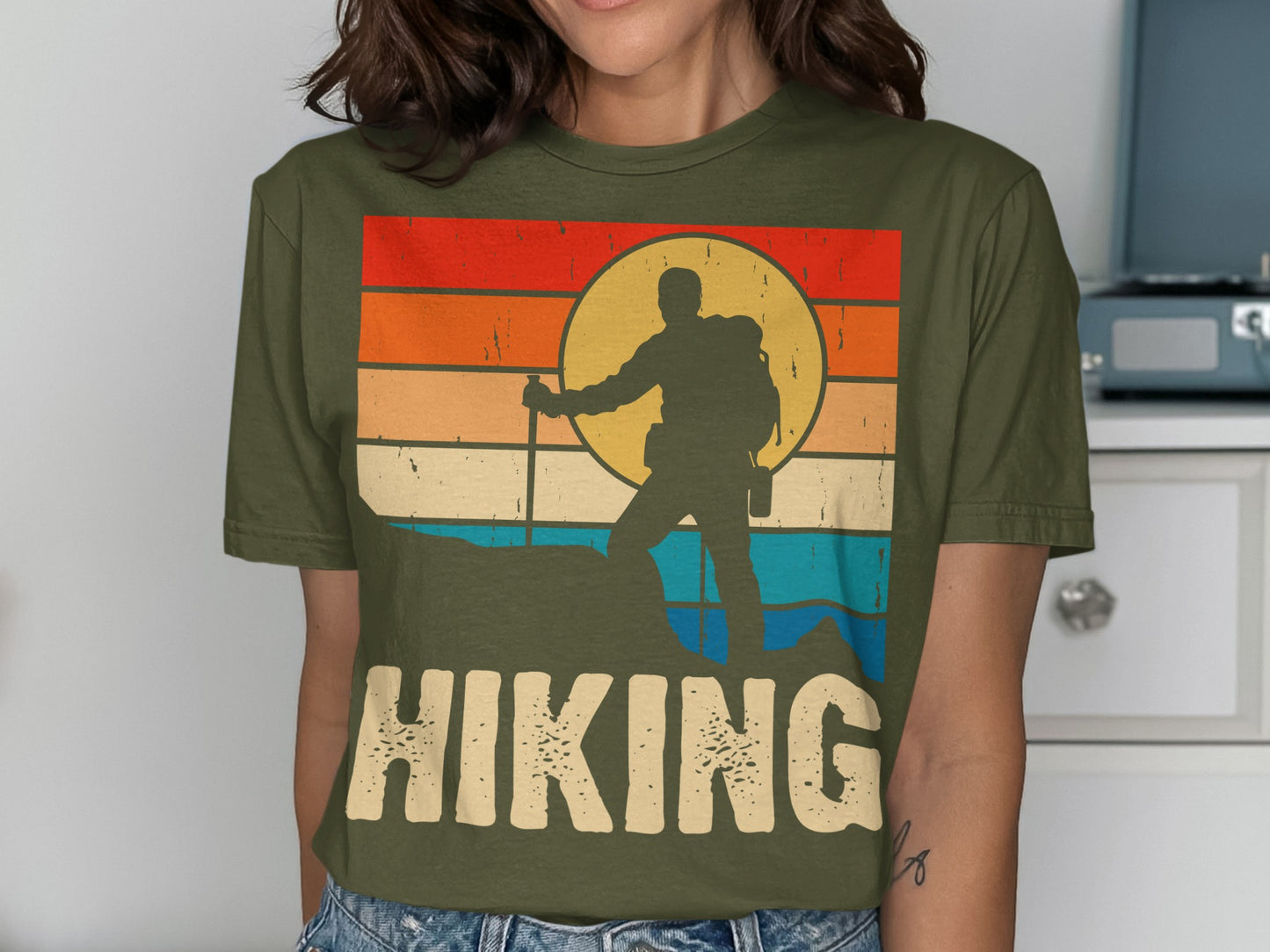 Hiking graphic on olive green t-shirt with sunset and mountain silhouette.
