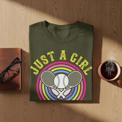 Olive green t-shirt with "JUST A GIRL" and tennis racquets and balls over rainbow circles.