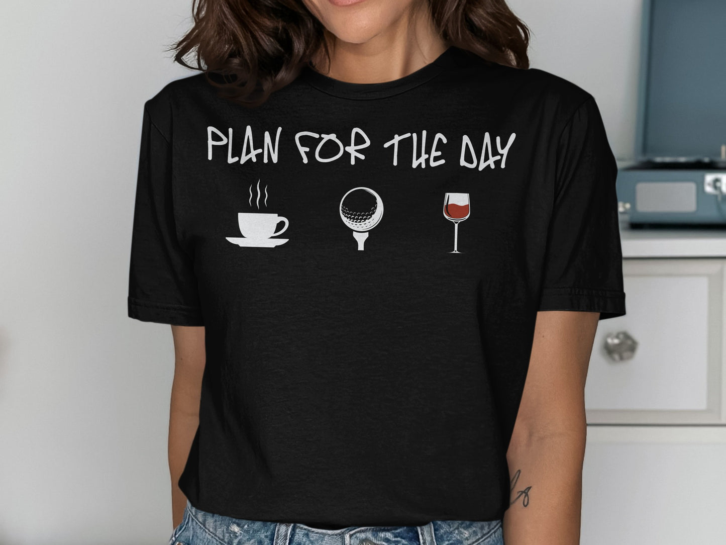 Black t-shirt with white icons: coffee cup, golf ball, wine glass, and text "PLAN FOR THE DAY".