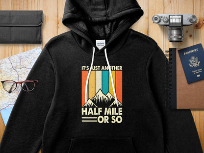 Black Gildan hoodie with "IT'S JUST ANOTHER HALF MILE OR SO" text and mountain graphic.