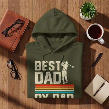 Green hoodie with "Best Dad" and golf design, flat lay on wood.