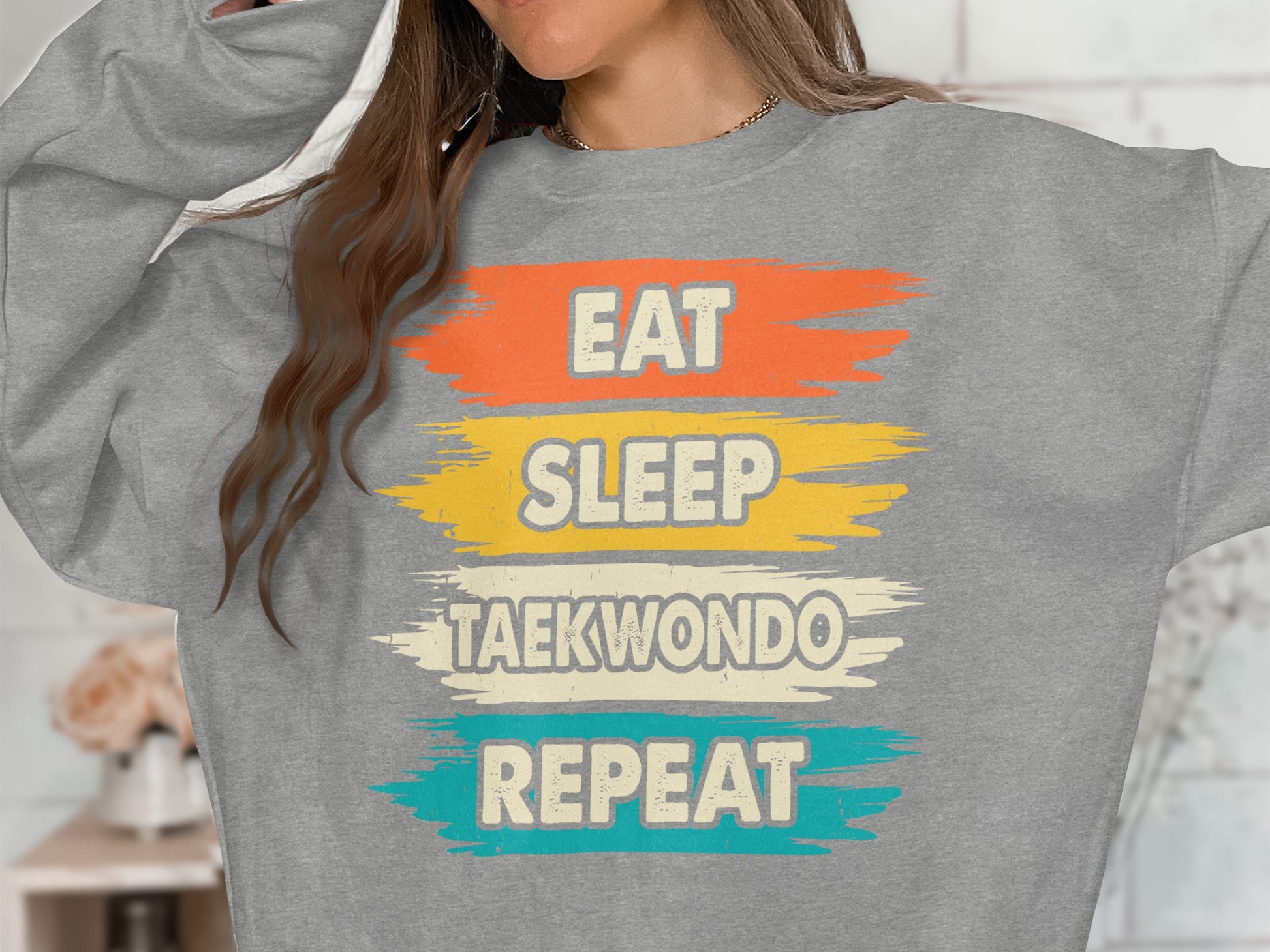 Grey sweatshirt with "EAT SLEEP TAEKWONDO REPEAT" in colorful painted text.