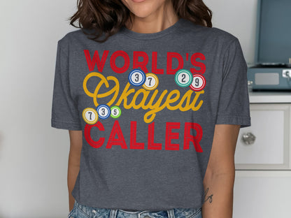 "World's Okayest Caller" text with bingo balls on a dark grey t-shirt.