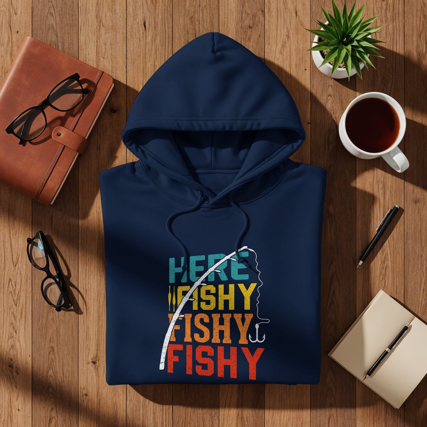 Navy hoodie with "Here Fishy Fishy" graphic, laid flat with accessories.