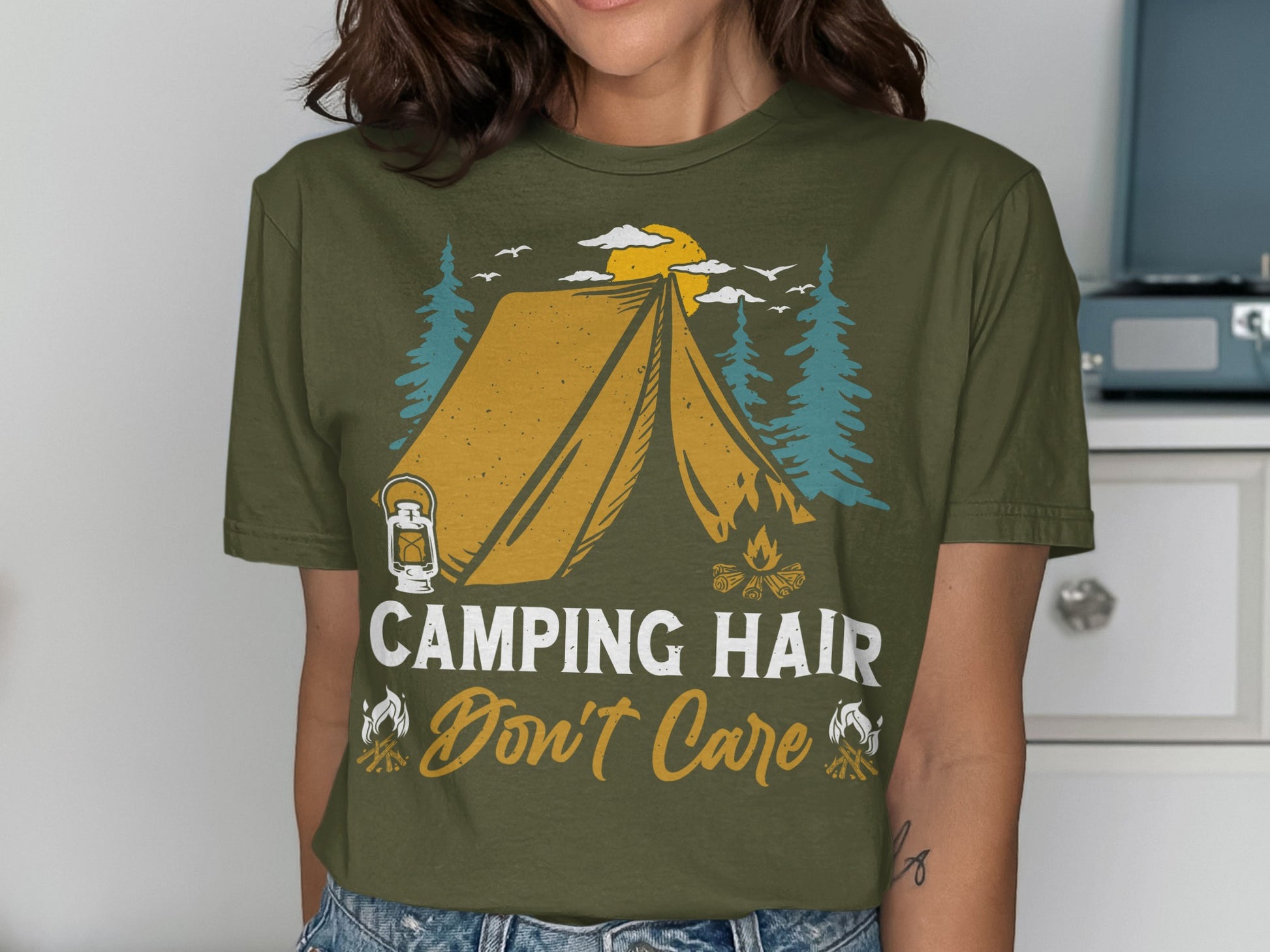 Olive green t-shirt with tent, campfire, trees, and "Camping Hair Don't Care" text.