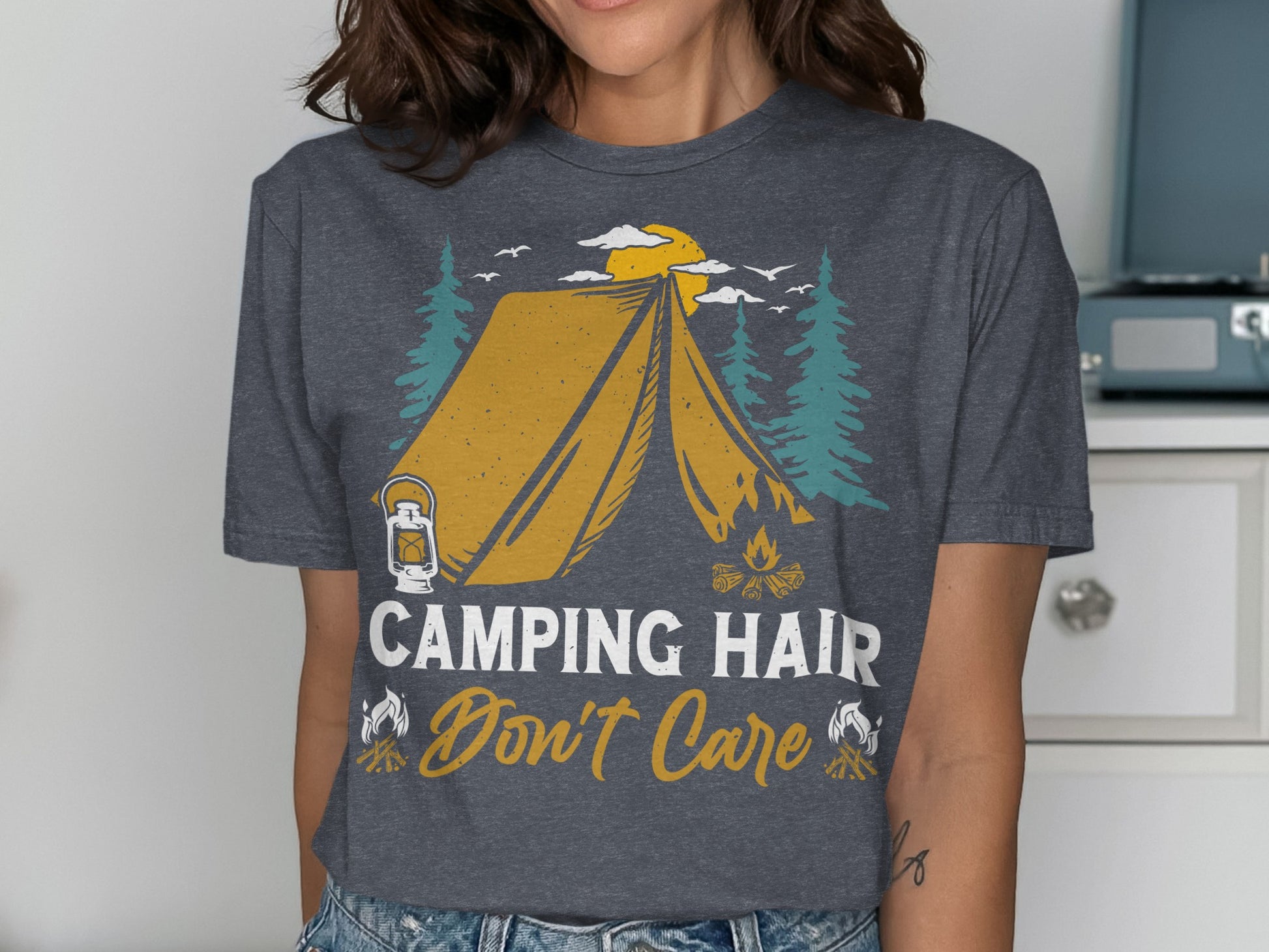 Graphic t-shirt with tent, campfire, trees, and text "Camping Hair Don't Care".