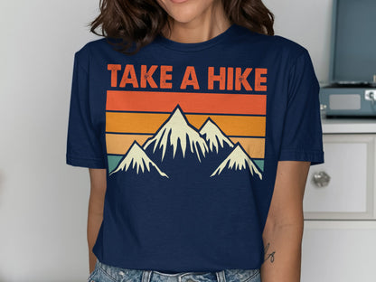 Navy t-shirt with mountains and text "TAKE A HIKE" against a sunset gradient.
