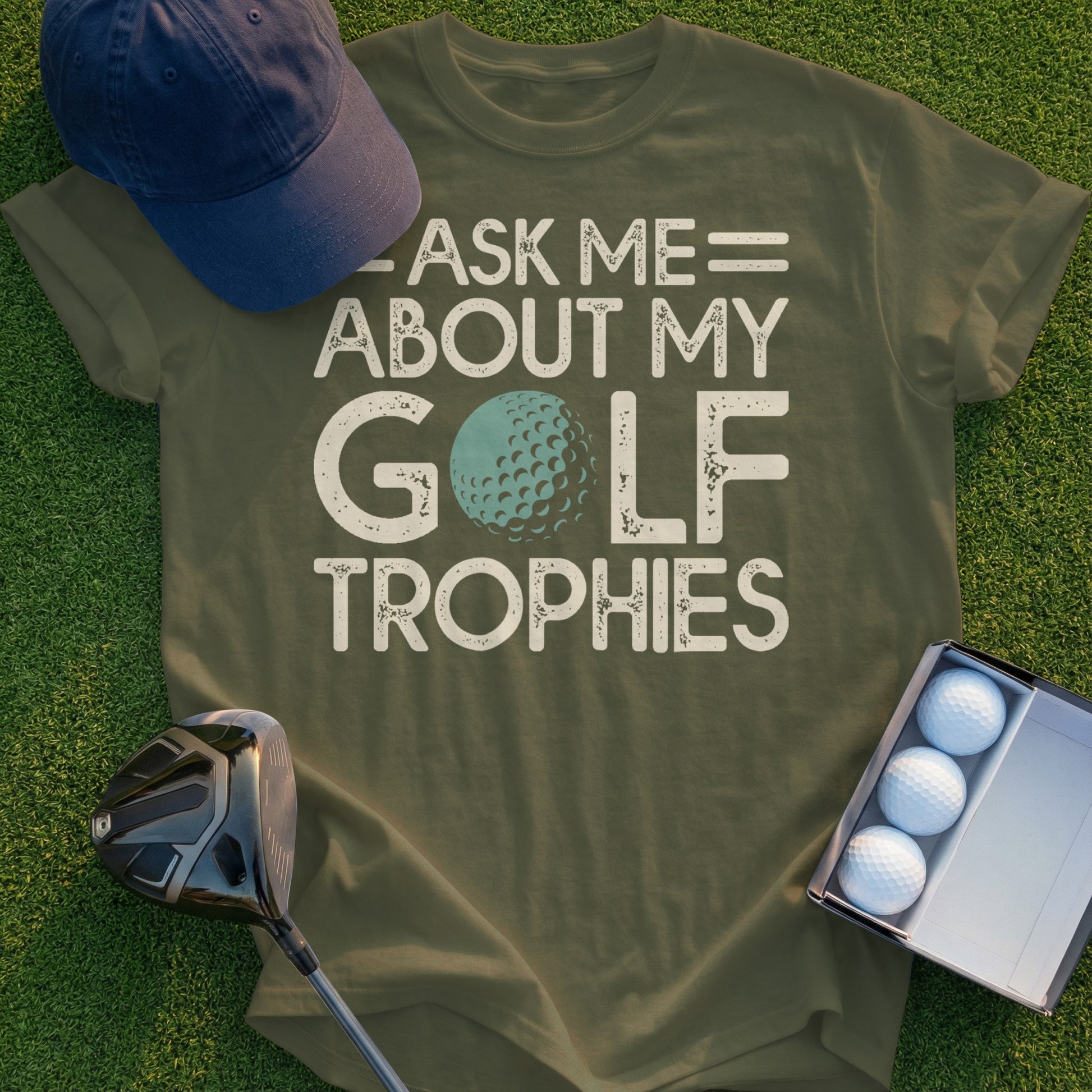 Olive green t-shirt with "ASK ME ABOUT MY GOLF TROPHIES" text and a golf ball.