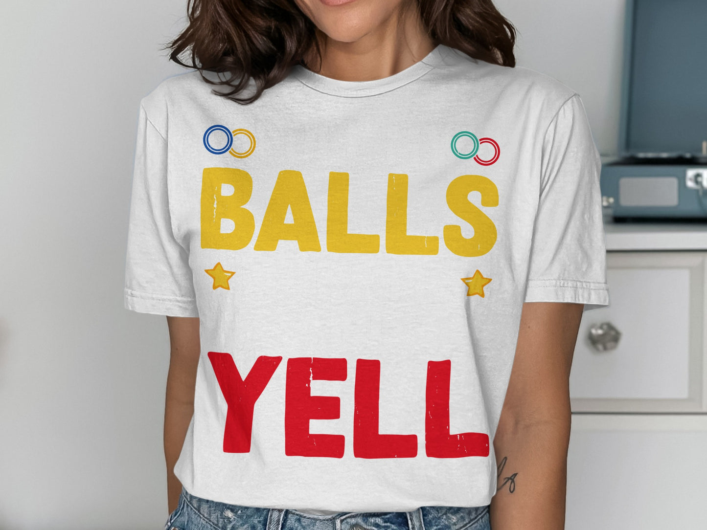 White t-shirt with "BALLS" in yellow and "YELL" in red, and Olympic rings.
