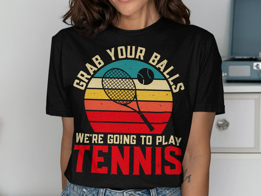 T-shirt with retro sunset design featuring tennis racket, ball, and "GRAB YOUR BALLS WE'RE GOING TO PLAY TENNIS".