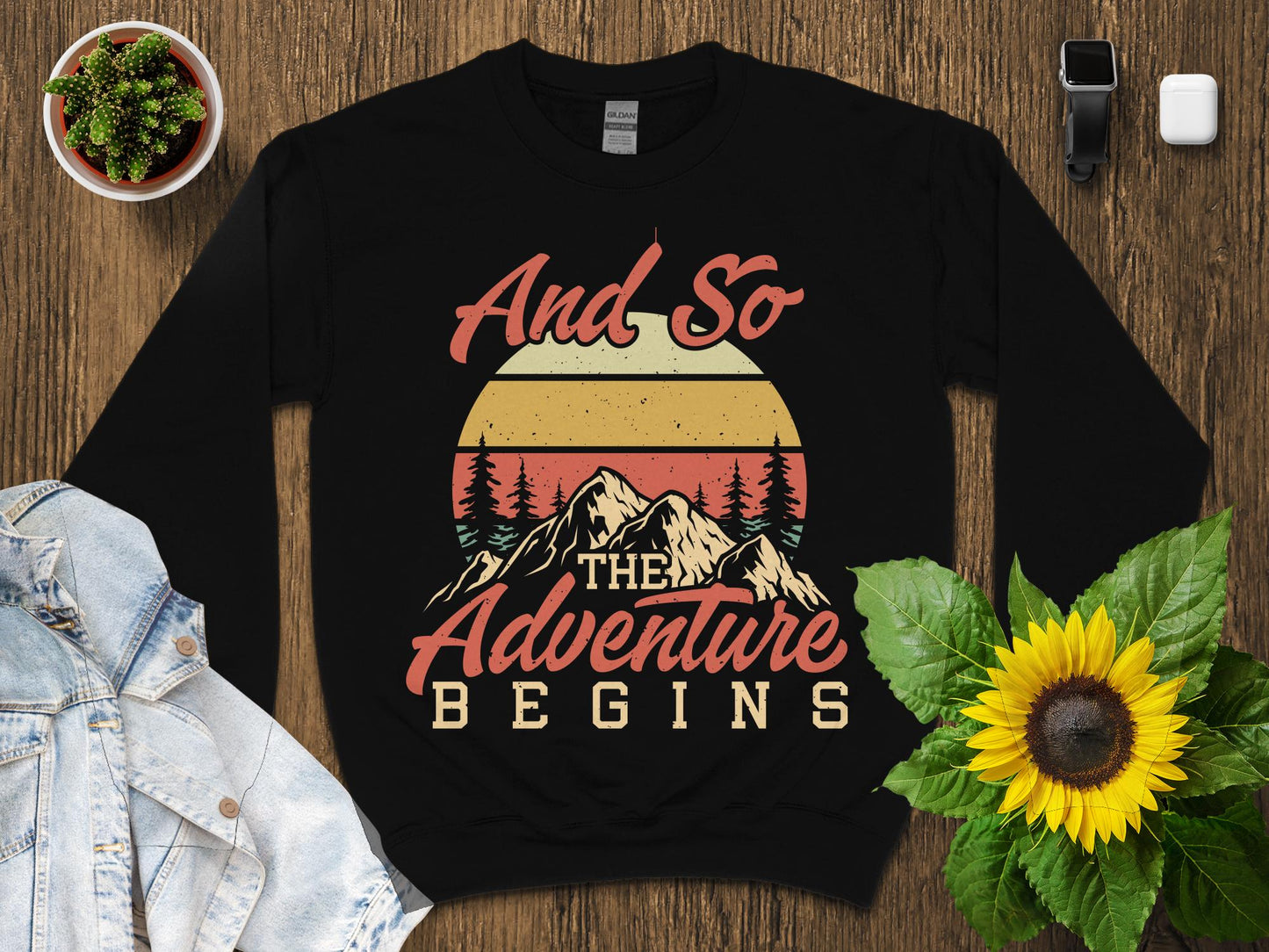 Black sweatshirt with "And So The Adventure Begins" graphic and mountain sunset design.