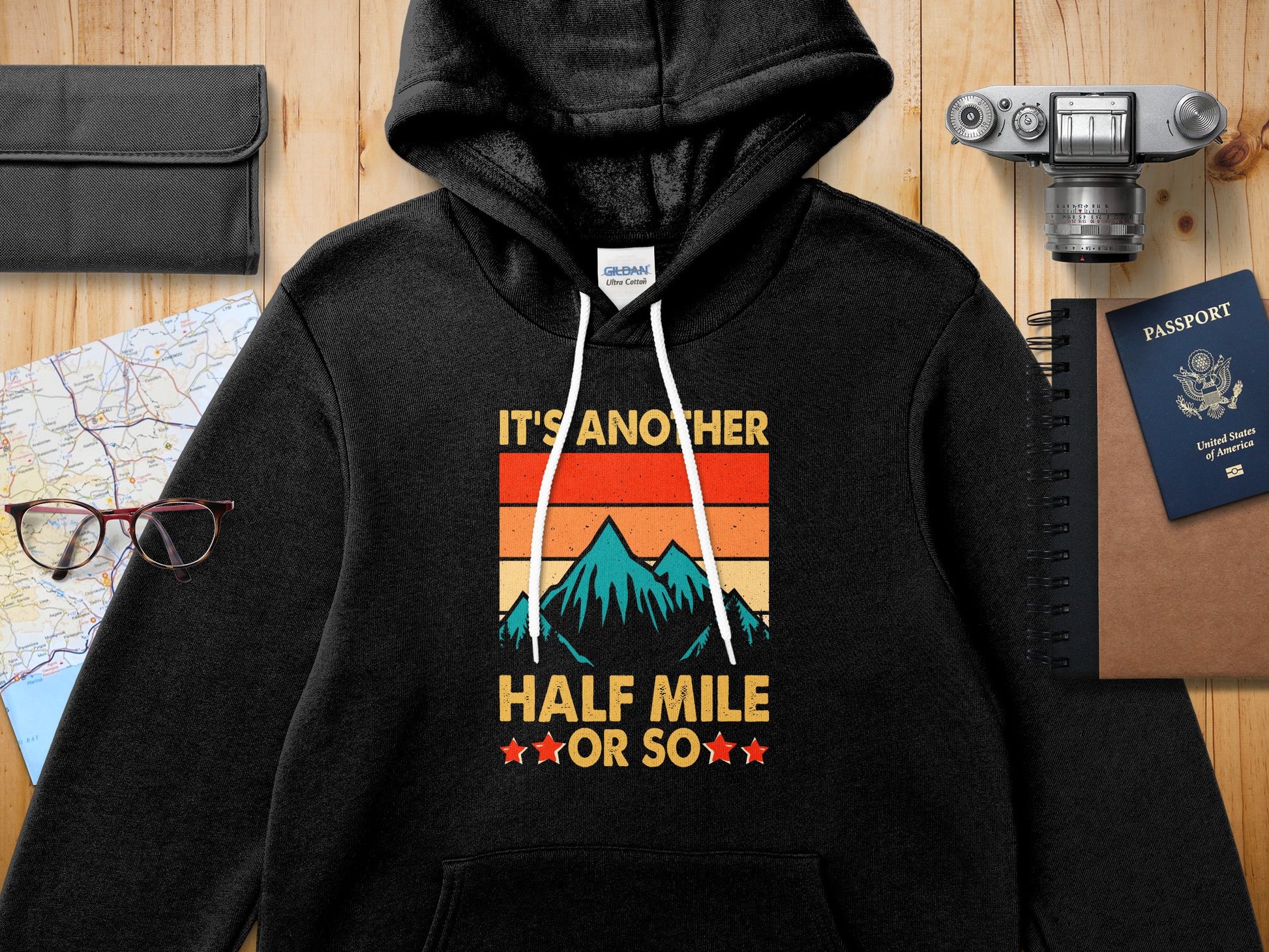 Black Gildan hoodie with "IT'S ANOTHER HALF MILE ★OR SO★" text and mountain graphic.