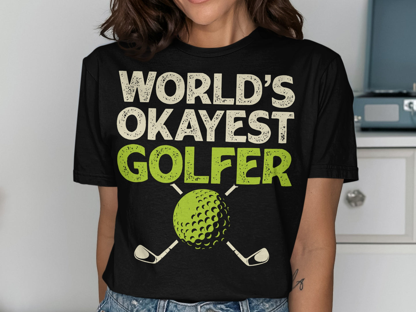 Black t-shirt with "World's Okayest Golfer" text and golf ball with clubs.