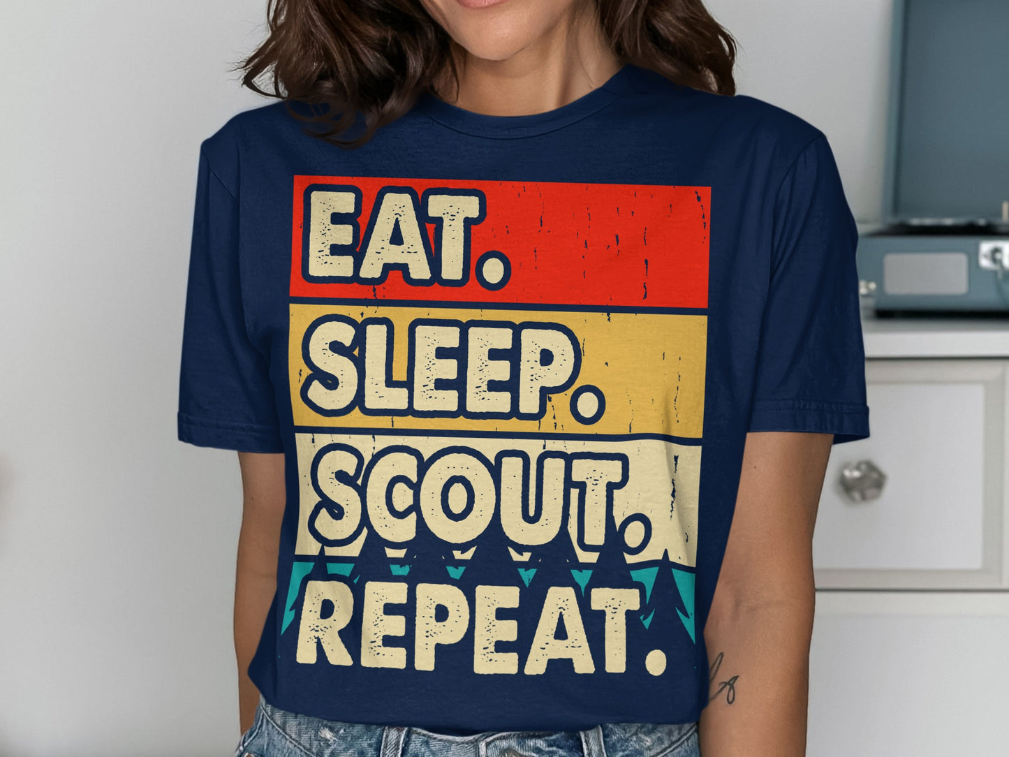 Navy t-shirt with bold "EAT. SLEEP. SCOUT. REPEAT." text on striped background.