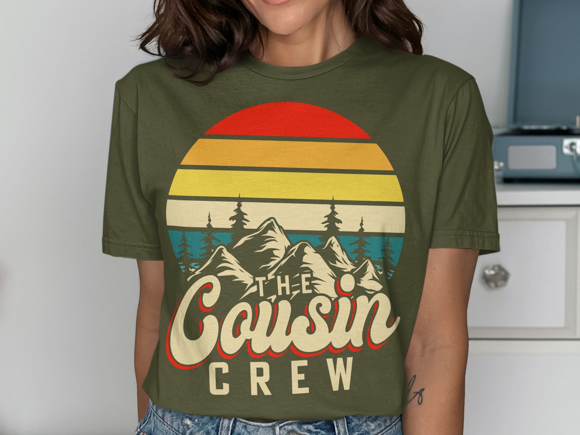 Olive green t-shirt with "The Cousin Crew" text and mountain sunset graphic.