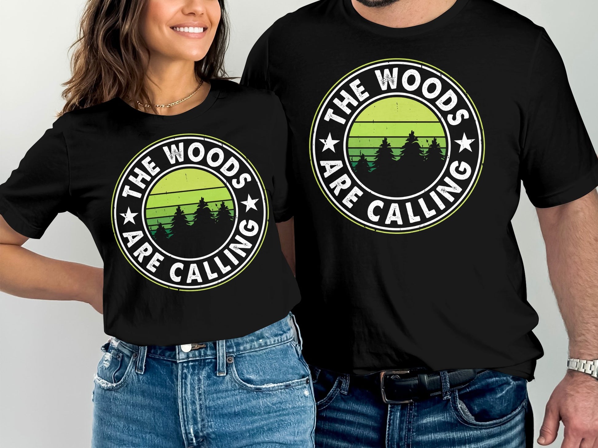 Two black t-shirts with "The Woods Are Calling" text and forest graphic.