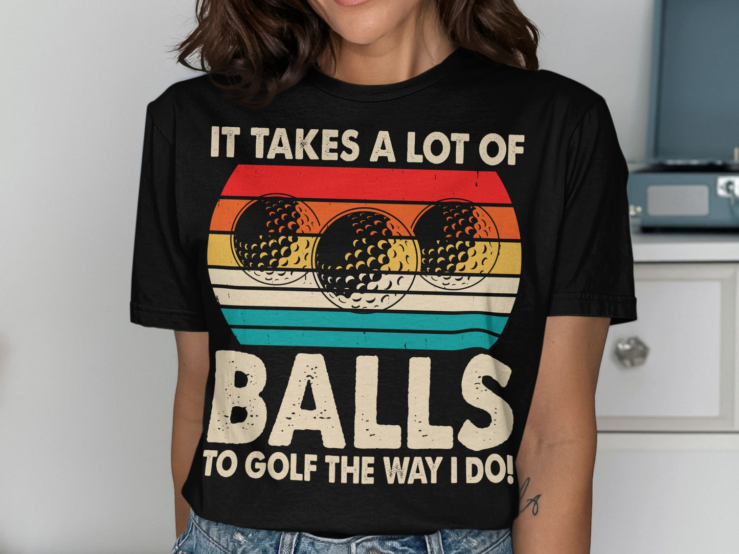 Black t-shirt with colorful striped background and "It Takes a Lot of Balls to Golf the Way I Do!" text.