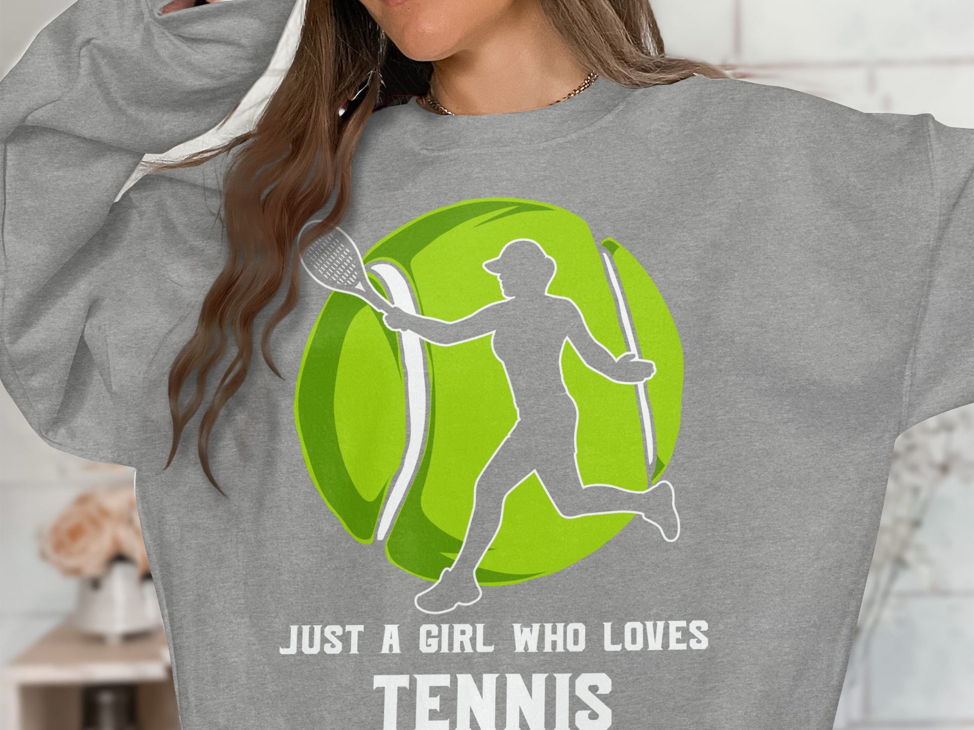 Woman in gray sweatshirt with graphic of tennis player and text "JUST A GIRL WHO LOVES TENNIS".