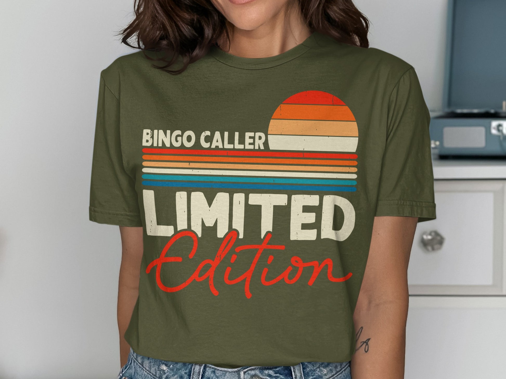 Olive green t-shirt with "BINGO CALLER" and "LIMITED Edition" text and a retro sunset graphic.